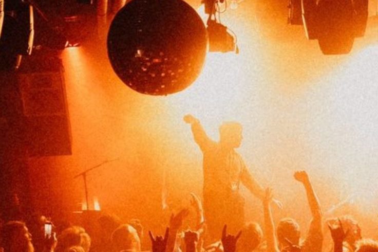 Público con las manos en alto bajo una bola de espejos en una fiesta electrónica