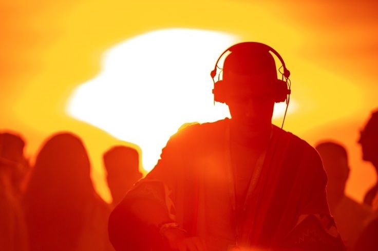 Silueta de un DJ con auriculares pinchando al atardecer frente al público